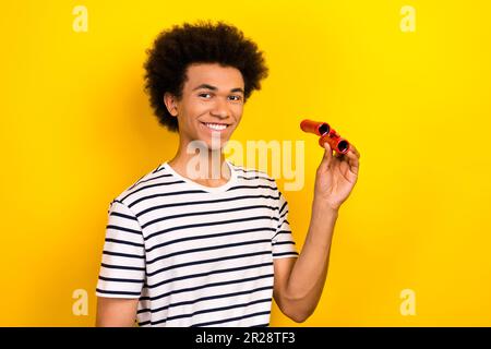 Portrait de jeune gai beau gars touriste tenir des lentilles jumelles antiques explorer la nature isolée sur fond jaune Banque D'Images