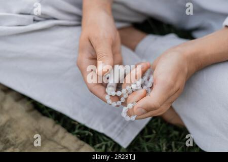 vue rognée d'un jeune homme tenant des perles de mala tout en méditant à l'extérieur Banque D'Images