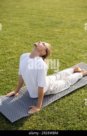 jeune homme barbu avec les yeux fermés méditant dans le cobra pose sur le tapis de yoga Banque D'Images