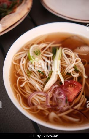 Bouillon pho, soupe vietnamienne dans une assiette profonde avec viande, bâtonnets chinois en bois et deux œufs de caille sur fond sombre Banque D'Images