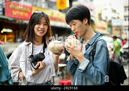 Chiang Mai, Thaïlande - 17 mai 2023: Heureux jeune couple de touristes asiatiques appréciant leur boisson fraîche à la noix de coco dans un quartier chinois à Chiang Mai. Banque D'Images