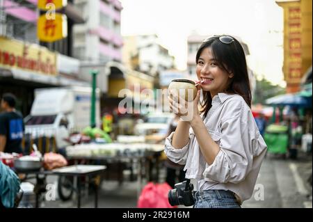 Chiang Mai, Thaïlande - 17 mai 2023: Heureuse et attrayante jeune asiatique touriste apprécie sa boisson fraîche de noix de coco tout en marchant autour de la ma de Chinatown Banque D'Images