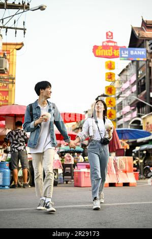 Chiang Mai, Thaïlande - 17 mai 2023 : un charmant jeune couple de touristes asiatiques qui tient les mains aime se promener dans la rue Chinatown de Chiang Mai ensemble. Banque D'Images