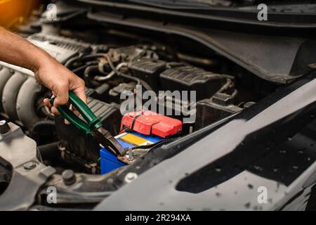 Gros plan, les mains d'un technicien masculin utilisent un outil pour remplacer la batterie de la voiture, garée à la maison. Voiture noire, la batterie est endommagée. Les outils ont du pli Banque D'Images