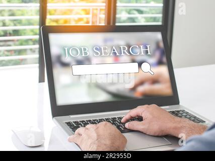 Un homme s'assoit et tape le clavier pour rechercher un emploi dans le travail à la maison. Trouvez du travail avec un ordinateur portable et placez-le sur la table blanche dans le salon. Conce Banque D'Images