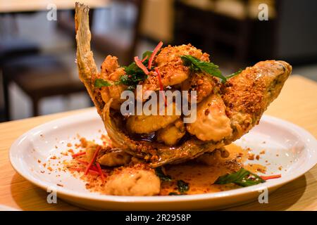 Bar de mer frits de 3 saveurs, piment clair, plaque blanche placée sur une table en bois, gros plan, arrière-plan flou Banque D'Images