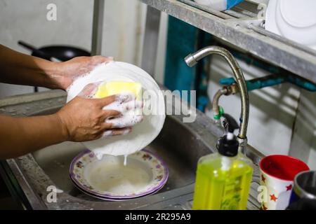 Gros plan et attention sélective sur les mains d'une femme qui lave la vaisselle et enlever les taches avec le liquide vaisselle dans la cuisine après le dîner. bba flou Banque D'Images
