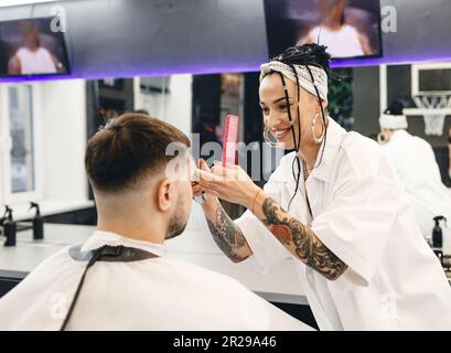 Une coiffeuse coupe les cheveux d'un homme dans un salon de coiffure. Salon de coiffure professionnel pour hommes. Salon de coiffure Banque D'Images