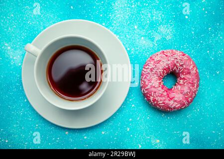 Beignet rose et une tasse de café sur fond bleu. Banque D'Images