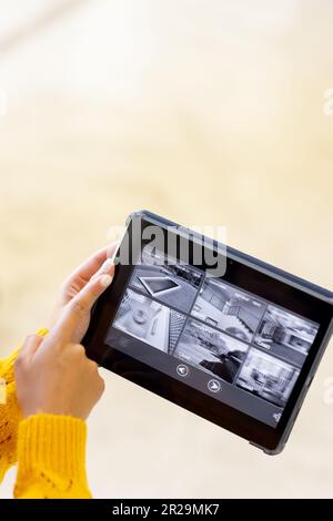 Mains d'une femme caucasienne tenant une tablette et pointant vers des vues de caméra de sécurité à l'écran, espace de copie Banque D'Images