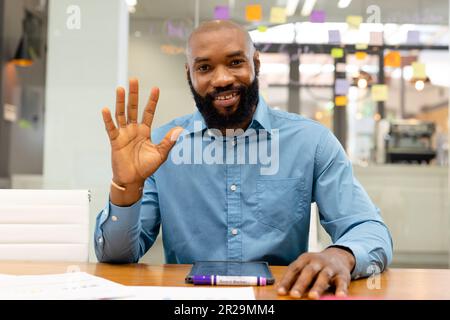 Portrait d'un homme d'affaires afro-américain barbu qui agite la main à son bureau Banque D'Images