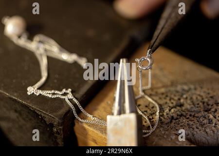Gros plan des mains de la travailleuse biraciale qui fait des bijoux à l'aide d'outils à l'atelier de bijoux Banque D'Images