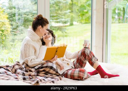 Belle fille et sa mère aiment le soleil matin. Bon moment à la maison ils s'assoient sur la véranda contre les fenêtres de fond avec une couverture et une tasse de café du matin concept relation entre les enfants et les parents Banque D'Images