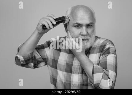 Portrait d'un homme âgé en train d'être tondu avec une tondeuse électrique professionnelle dans un salon de coiffure, coupe de cheveux avec un rasoir électrique. Banque D'Images