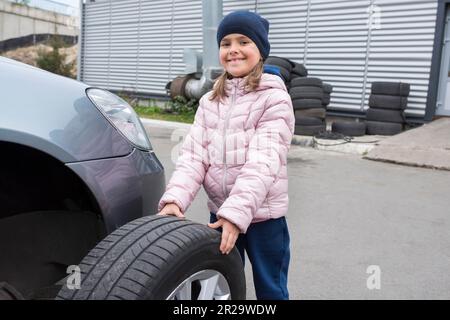 Portrait d'une fille de 6 ans avec une roue de voiture dans les mains. Service de voiture. Service de réparation Banque D'Images