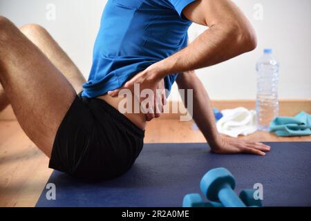 Détail de l'homme faisant du sport avec douleur lombaire se tenant avec sa main assise sur un tapis. Vue latérale Banque D'Images