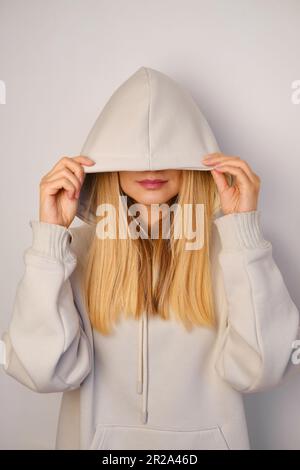 Jeune belle fille dans un blanc à capuchon posant. Pull à capuche ultra-large chaud avec capuche. Noeud tendance. Essayer de porter des vêtements en magasin. Sous-culture de la jeunesse Banque D'Images