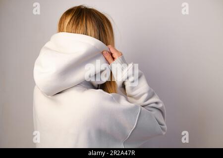 Jeune belle fille dans un blanc à capuchon posant. Pull à capuche ultra-large chaud avec capuche. Noeud tendance. Essayer de porter des vêtements en magasin. Sous-culture de la jeunesse Banque D'Images