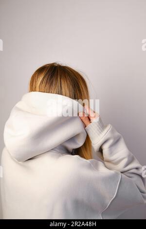 Jeune belle fille dans un blanc à capuchon posant. Pull à capuche ultra-large chaud avec capuche. Noeud tendance. Essayer de porter des vêtements en magasin. Sous-culture de la jeunesse Banque D'Images