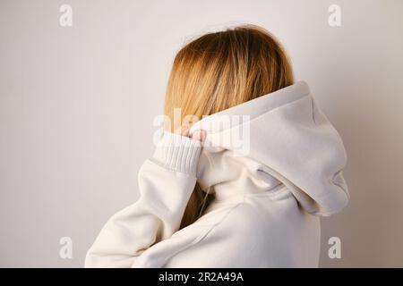 Jeune belle fille dans un blanc à capuchon posant. Pull à capuche ultra-large chaud avec capuche. Noeud tendance. Essayer de porter des vêtements en magasin. Sous-culture de la jeunesse Banque D'Images