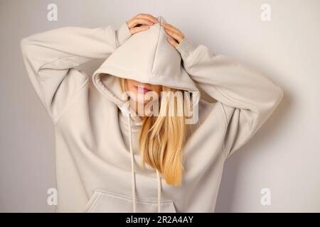 Jeune belle fille dans un blanc à capuchon posant. Pull à capuche ultra-large chaud avec capuche. Noeud tendance. Essayer de porter des vêtements en magasin. Sous-culture de la jeunesse Banque D'Images