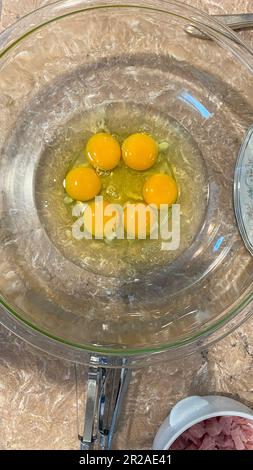 Vue en hauteur de six œufs crus avec jaune d'œuf non cassé dans un bol transparent sur un comptoir de cuisine. Banque D'Images