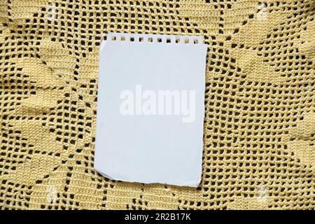 une feuille de papier blanche vierge avec un bloc-notes repose sur une serviette en dentelle jaune, espace pour le texte Banque D'Images