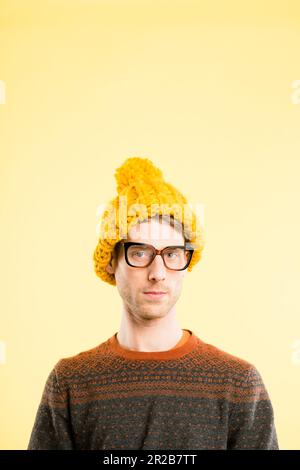 Umm, quoi. un beau jeune homme debout seul dans le studio et posant tout en portant un bonnet et des lunettes. Banque D'Images