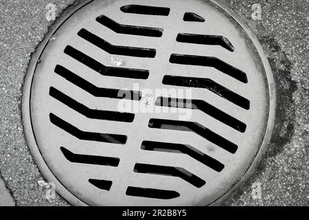 Un trou d'égout, une petite porte d'accès à un labyrinthe souterrain, se trouve de façon évidente dans la rue. Sa couverture épaisse dissimule un réseau de tuyaux . Banque D'Images