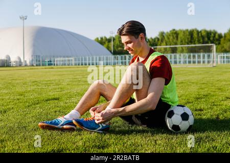 Un jeune joueur de football masculin noue des lacets sur le terrain de football Banque D'Images