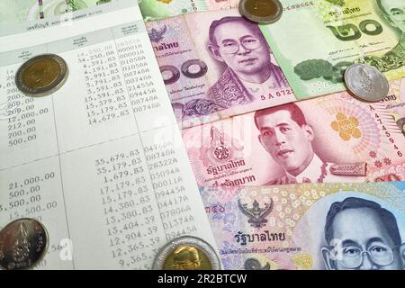 Gros plan sur un livret avec quelques pièces et billets thaïlandais bains. Le livret est écrit en thaï, en chinois et en anglais. Banque D'Images