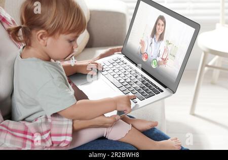 Mère et fille ayant une consultation en ligne avec le pédiatre via ordinateur portable sur le canapé à la maison Banque D'Images