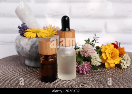 Bouteilles en verre d'huile essentielle, mortier avec pilon et différentes fleurs sauvages sur tapis en osier Banque D'Images