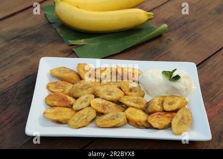 De savoureuses tranches de banane frite avec de la crème glacée et de la menthe sur une table en bois Banque D'Images