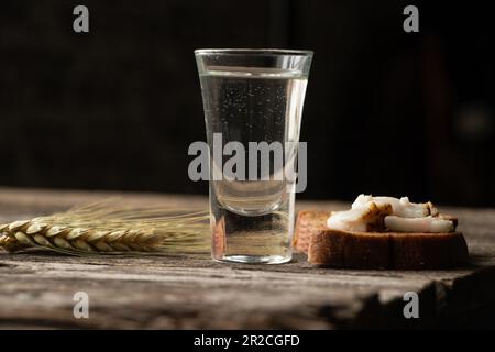 Un verre de vodka à côté d'un morceau de pain noir avec du bacon sur une table en bois dans la cuisine pour le déjeuner en ukrainien Banque D'Images