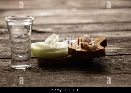 Un verre de vodka à côté d'un morceau de pain noir avec du bacon sur une table en bois dans la cuisine pour le déjeuner en ukrainien Banque D'Images