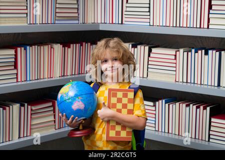 Garçon d'école avec le monde et les échecs, l'enfance. Concept d'école et d'éducation. Portrait d'un enfant garçon scolaire mignon. Retour à l'école. Banque D'Images