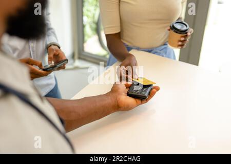 Mi-section de client afro-américain lisant la carte de crédit sur le lecteur de code-barres détenu par le barista Banque D'Images