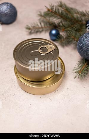 Produits de Noël, conserves de conservation, poisson emballé, viande ou légumes en boîte sur fond gris en béton avec arbre de Noël et balles de jouet. Copier Banque D'Images