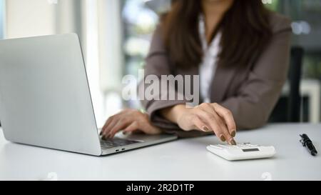 Gros plan d'une femme d'affaires ou d'une comptable qui utilise une calculatrice pour calculer les données financières, travaillant à son bureau. Banque D'Images