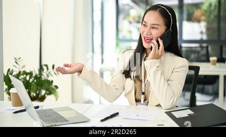 Femme d'affaires asiatique attirante et professionnelle du millénaire qui fait des affaires par téléphone avec sa cliente à son bureau. Banque D'Images