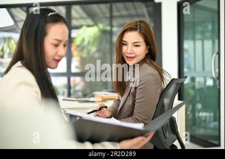Femme d'affaires asiatique du millénaire attrayante et professionnelle qui donne des conseils et partage ses idées sur le travail de son collègue au bureau. Banque D'Images