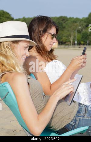 femme et sœur utilisant une tablette et un téléphone à la mer Banque D'Images