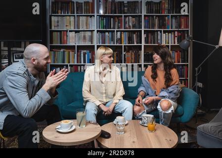 Heureux groupe diversifié d'étudiants de collège travaillant ensemble sur le projet d'étude dans la bibliothèque de l'université, assis à la table avec des livres, ordinateur portable, discutant discussi Banque D'Images