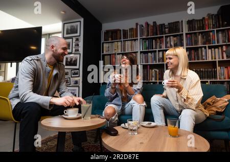 Heureux groupe diversifié d'étudiants de collège travaillant ensemble sur le projet d'étude dans la bibliothèque de l'université, assis à la table avec des livres, ordinateur portable, discutant discussi Banque D'Images