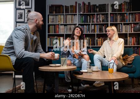 Heureux groupe diversifié d'étudiants de collège travaillant ensemble sur le projet d'étude dans la bibliothèque de l'université, assis à la table avec des livres, ordinateur portable, discutant discussi Banque D'Images