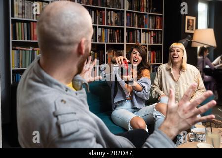 Heureux groupe diversifié d'étudiants de collège travaillant ensemble sur le projet d'étude dans la bibliothèque de l'université, assis à la table avec des livres, ordinateur portable, discutant discussi Banque D'Images