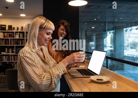 Une jeune fille étudiante gaie montrant la présentation en ligne d'apprentissage sur ordinateur portable à classmate, tenant le gadget numérique, regardant l'écran, souriant, utilisant Banque D'Images