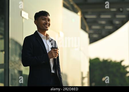 Portrait d'un homme d'affaires réussi tenant une tasse à café à emporter devant le bâtiment de bureau avec la lumière du soleil tôt le matin Banque D'Images