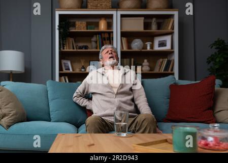 L'homme âgé à cheveux gris âgé à visage rouge âgé se wirthes dans la douleur souffre de la faible tension du dos, le frottement au toucher ou le massage de la longe réduit le mal de dos. Disque dégénératif Banque D'Images